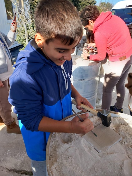 A child in a blue jacket using a hammer and chisel on a stone block. 2