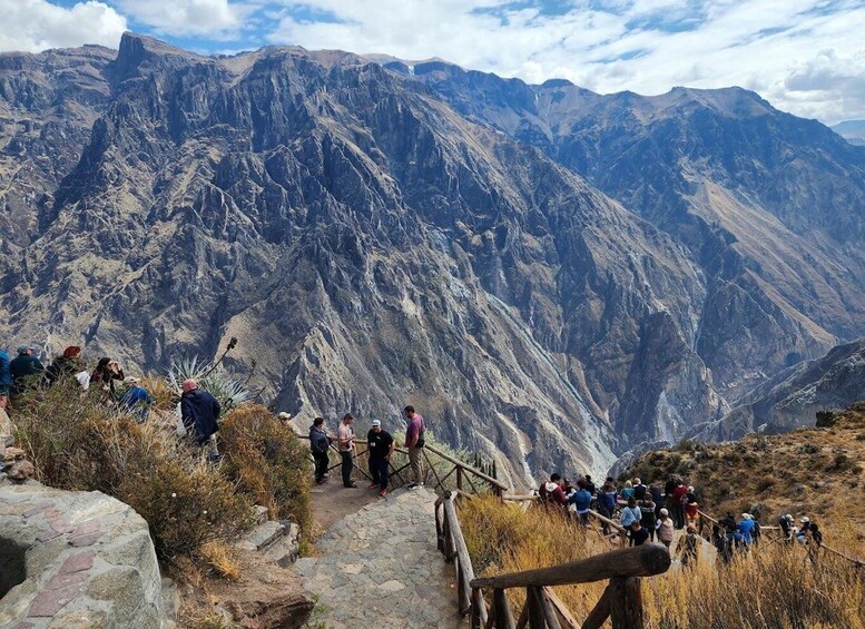 A group of hikers on a mountain trail with steep rocky terrain and a valley in the background. 3