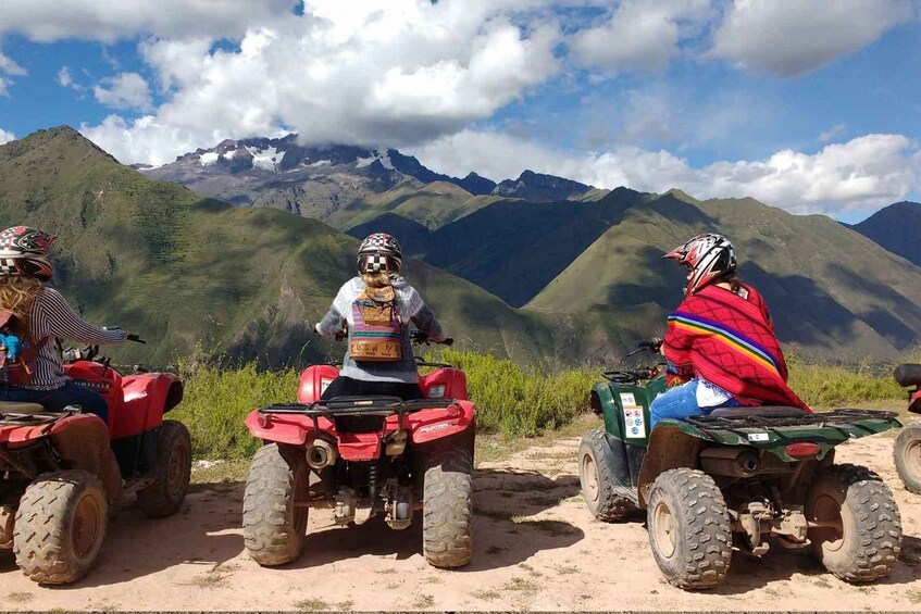Three people on ATVs in a mountainous area with green hills and a clear sky. 1