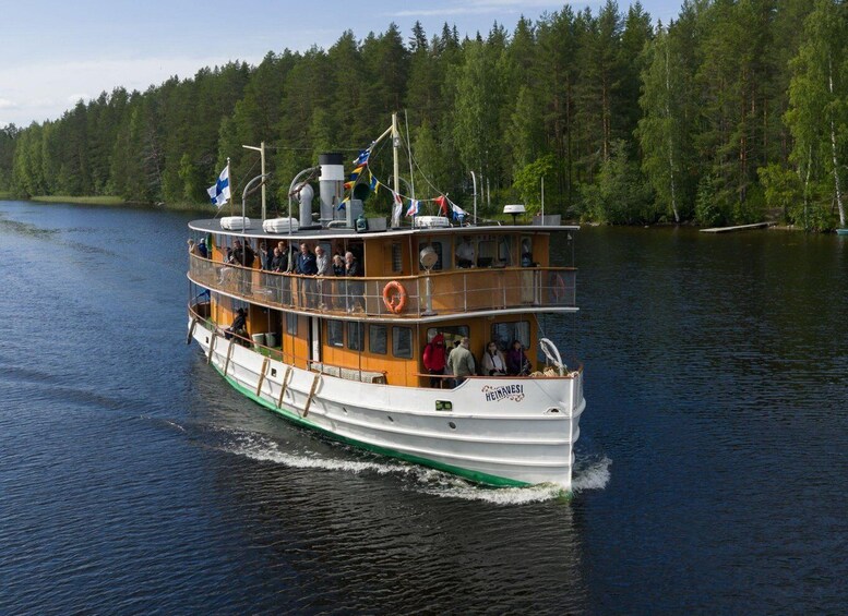 A multi-deck boat named 'HEINAVESI' on a calm lake surrounded by dense forest. 5