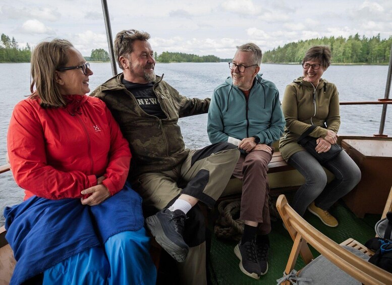 Four people sitting on a boat with a lake and forest in the background. 4