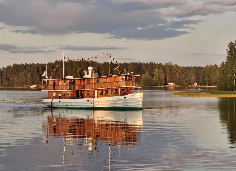 A multi-deck boat on calm water with a forested shoreline in the background. 1