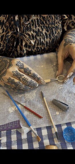 A tattoo artist working on a client's hand with various tattooing tools and a grid pattern on the table. 2