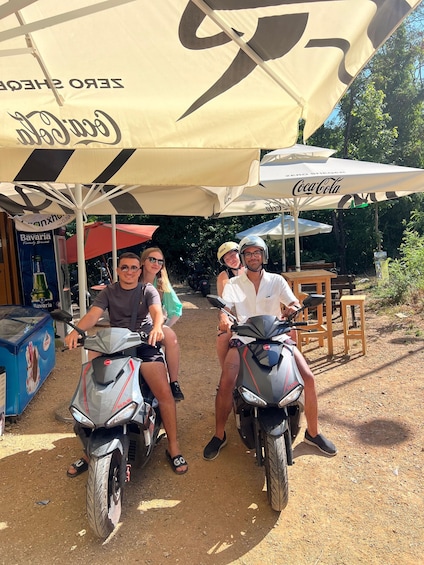 Four people on scooters under Coca-Cola branded umbrellas. 1