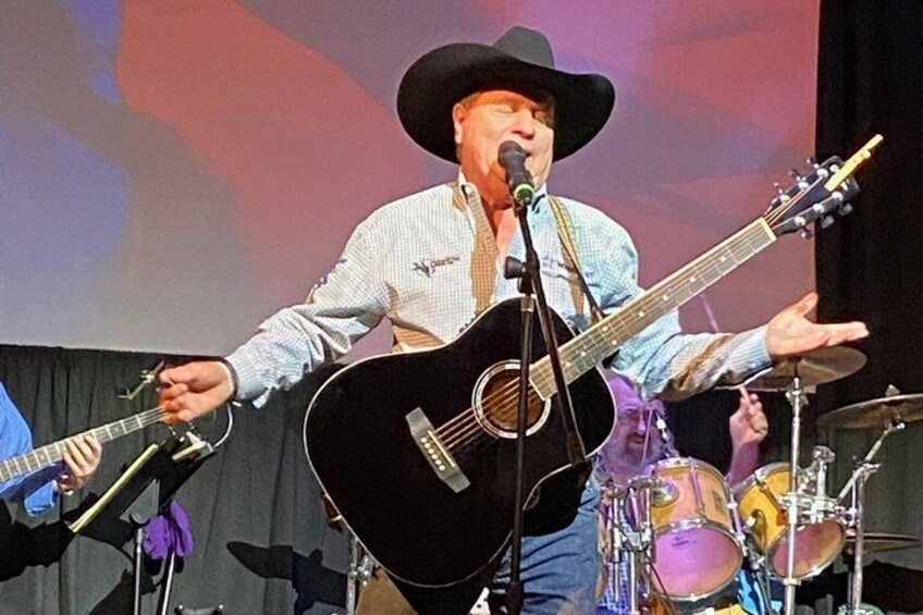A person playing an acoustic guitar on stage with a microphone. 2