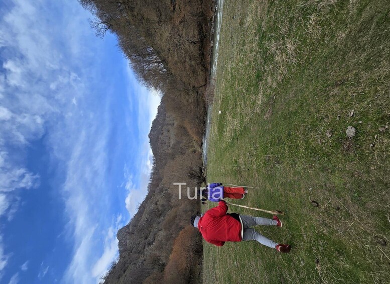 A person hiking in a grassy area with a river and mountains in the background. 4