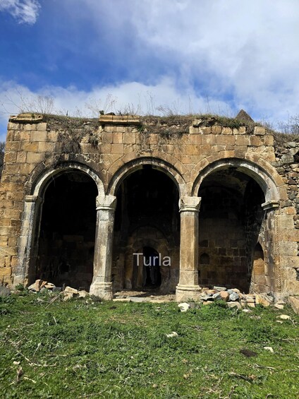 An ancient stone structure with three arched doorways and the word 'Turla' visible on the wall. 3
