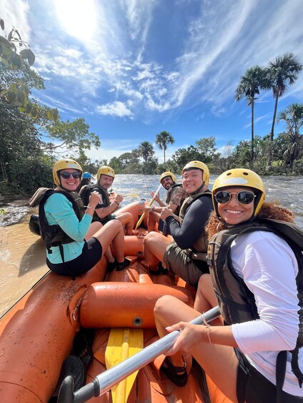 A group of people in a raft on a river surrounded by palm trees. 1