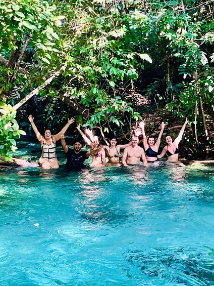 A group of people in a clear blue pool surrounded by lush greenery. 2