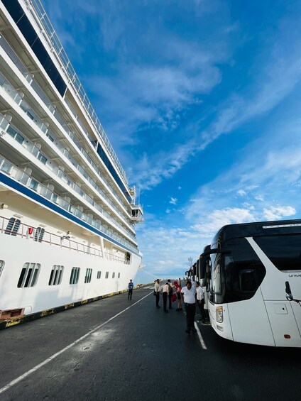 A large cruise ship docked at a port with a bus and people boarding. 5