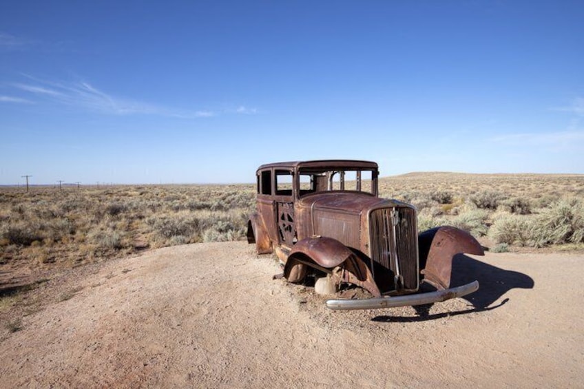 An old, rusted car in a desert landscape. 1