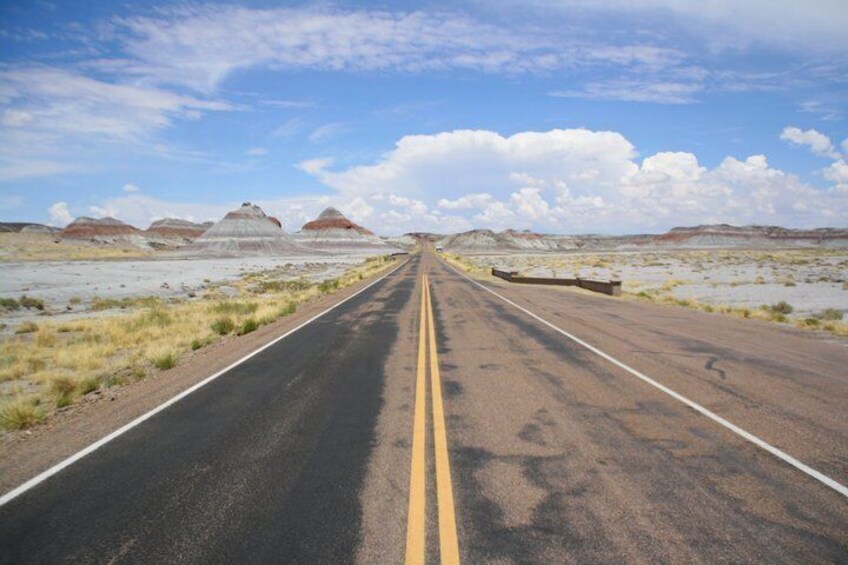 A straight road with yellow centerline, surrounded by flat terrain and distant hills. 5