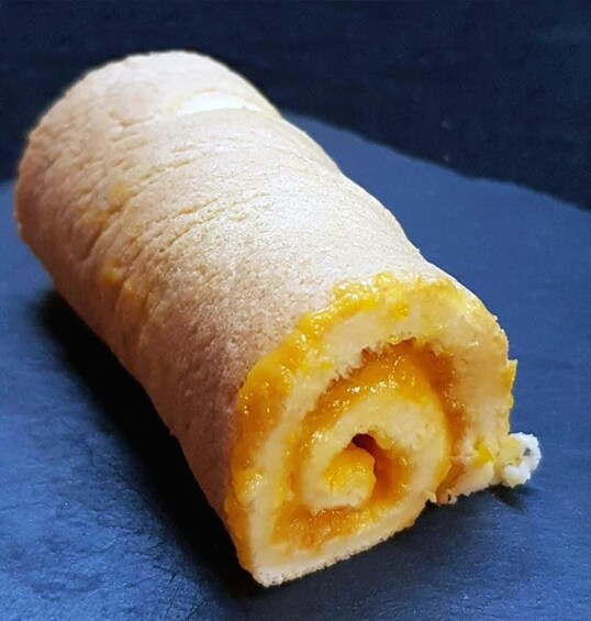 Rullattu leivonnainen, jonka täyte on kullanruskeaa, asetettu tummalle alustalle. 2