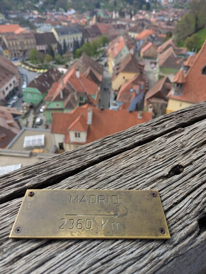 A plaque on a wooden railing with 'MADRID 2360 Km' engraved on it, overlooking a cityscape. 5
