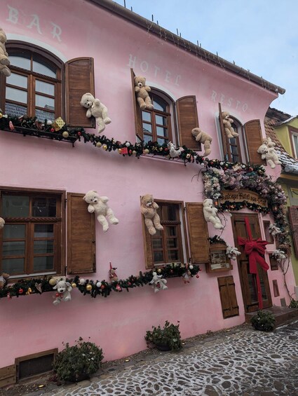 A pink building with multiple windows adorned with teddy bears and Christmas decorations. 1