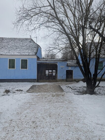 A snow-covered building with a tiled roof, a wooden door, and a tree in the foreground. 2
