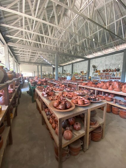 A pottery workshop with shelves of clay pots and a metal roof structure. 3