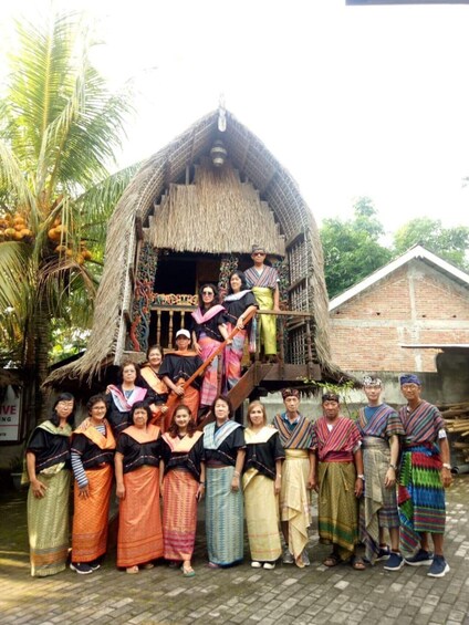 A group of people in traditional attire standing in front of a thatched-roof house with a sign reading 'ST. THOMAS.' 2