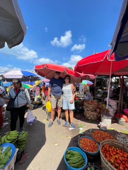 A market with people shopping under red umbrellas, various fruits and vegetables on display. 5