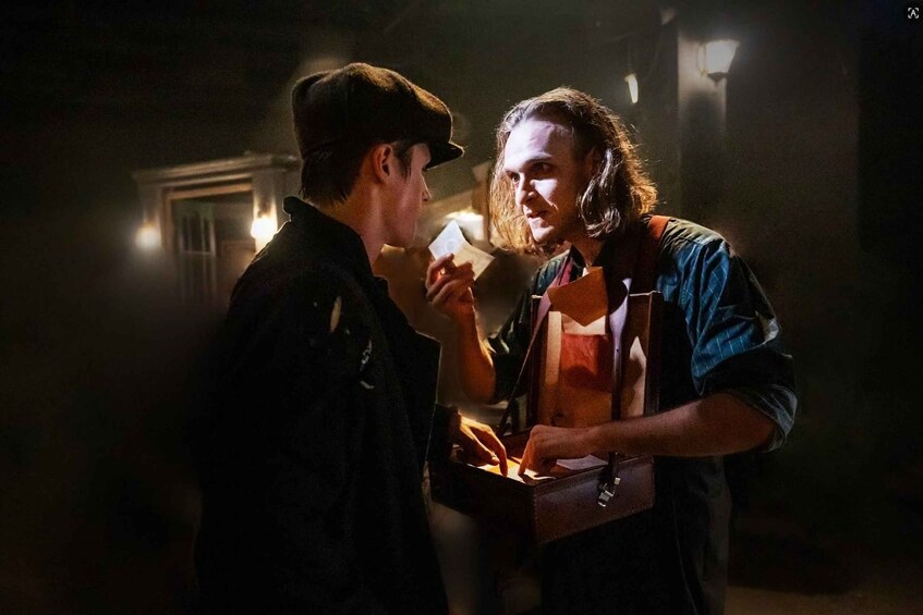 Two people in a dimly lit setting, one handing over a card to the other. 4