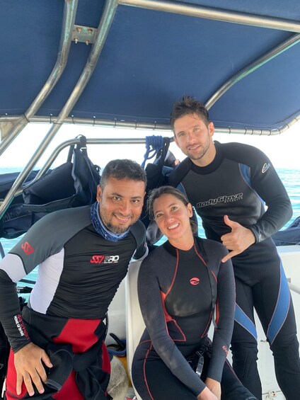 Three people in wetsuits on a boat. 1