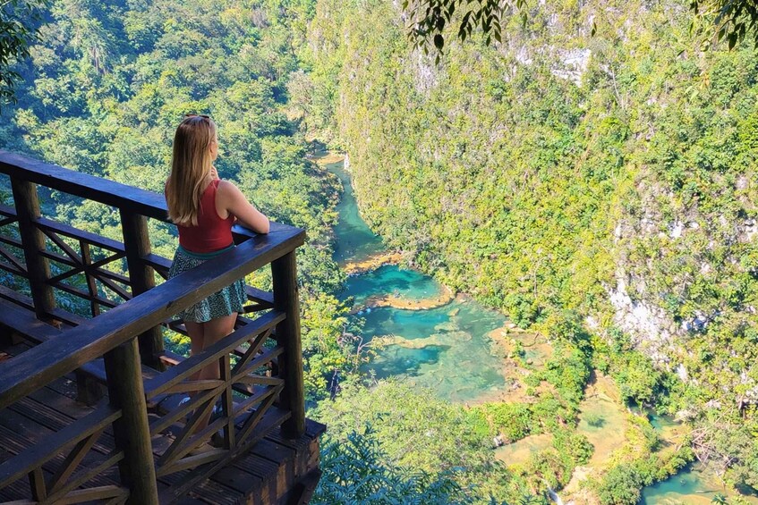 A woman standing on a wooden deck overlooking a river surrounded by dense forest. 1