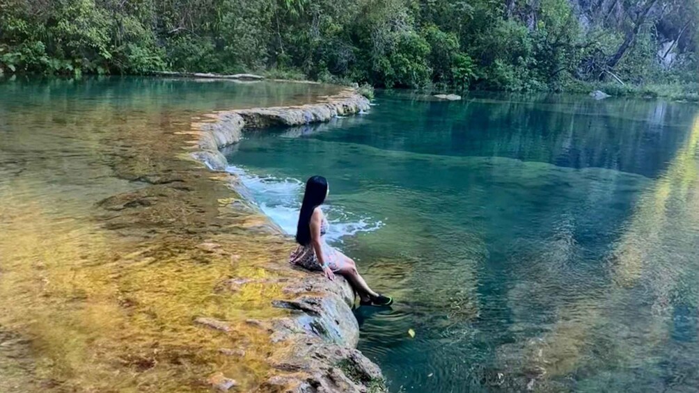 A person sitting on a rock by a clear river surrounded by greenery. 2