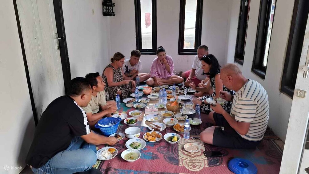 A group of people sitting on the floor around a table with various dishes and drinks. 2