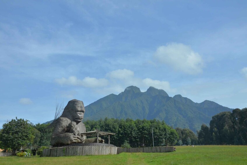 A large stone gorilla statue in a grassy field with a mountain in the background. 3