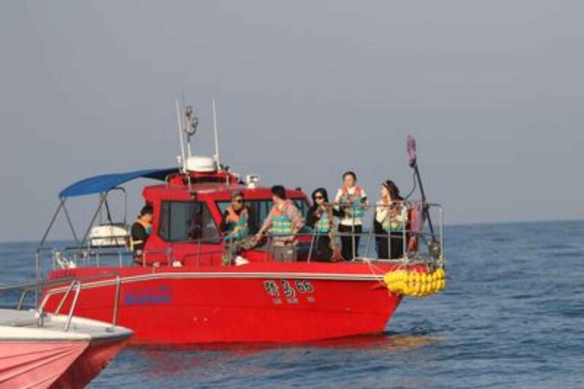 A red boat with passengers on board, floating on calm water. 3