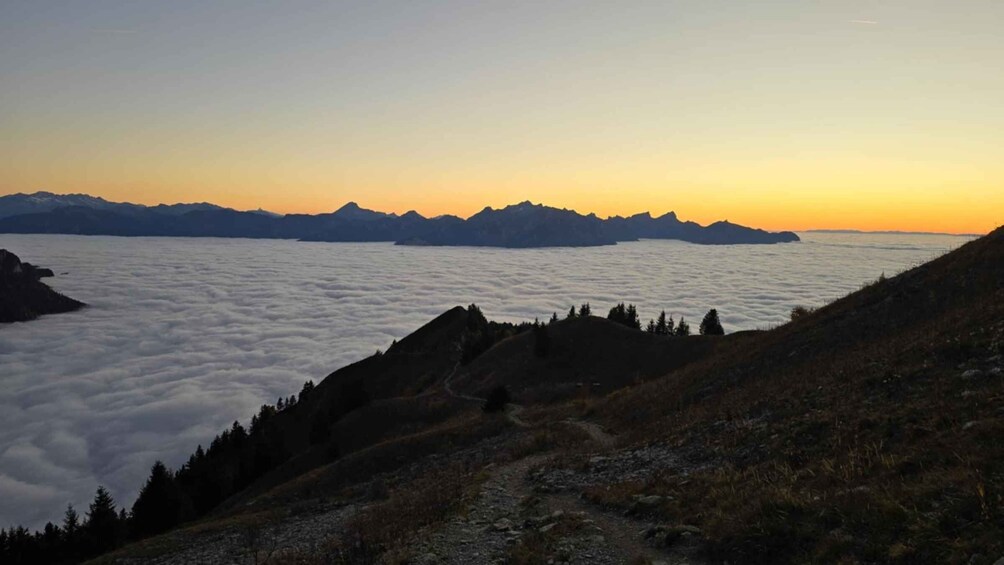 A mountain landscape at sunrise with a view of the sea below and a path leading up the hill. 5
