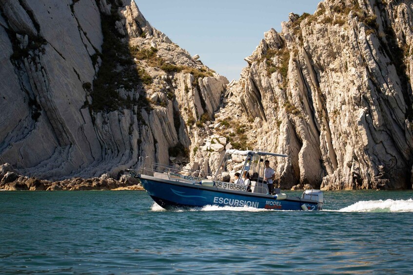 A boat named 'ESCURSIONI' with 'MODEL' written on it, navigating through a narrow waterway flanked by rocky cliffs. 3