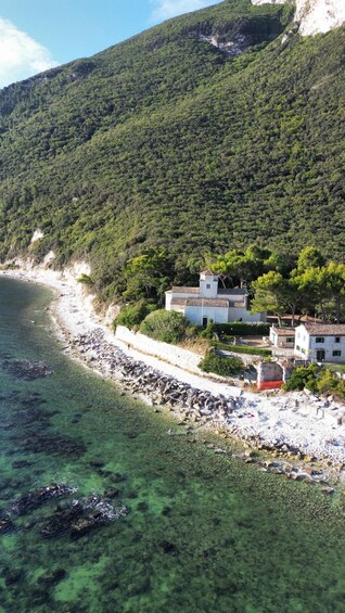 A coastal village with buildings near the beach, surrounded by dense forest and a clear blue sea. 2