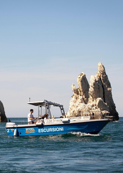 A boat named 'ESCURSIONI' with a person steering it, near a rocky coastline. 1