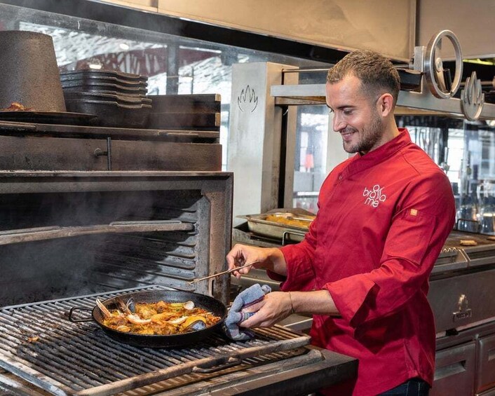 A chef in a red uniform cooking on a grill with a pan. 1