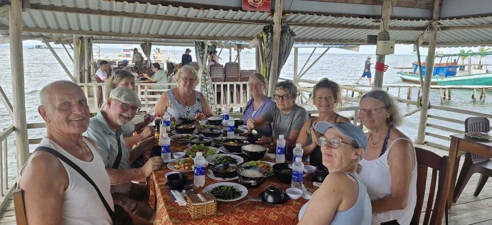 A group of people dining at a table on a boat with various dishes and drinks. 3