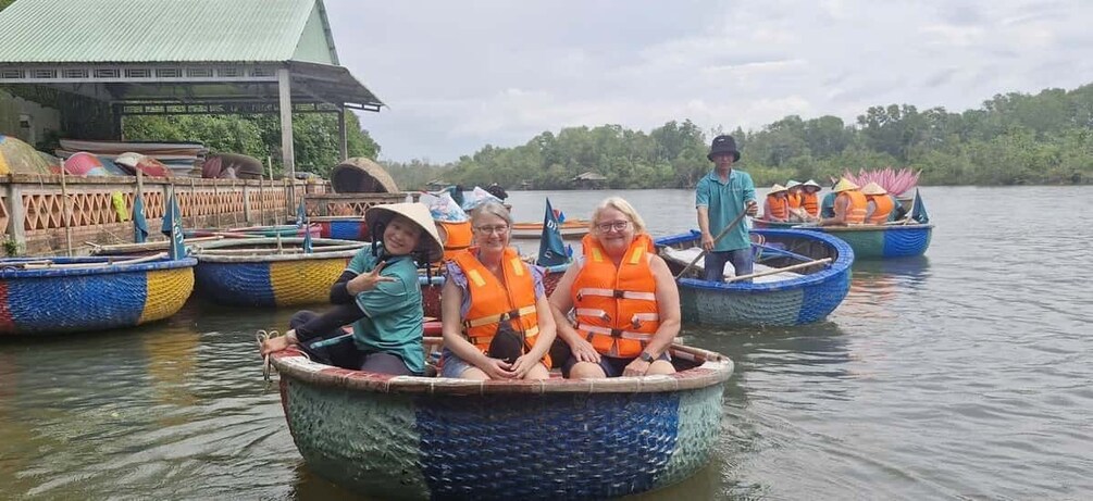 People in a boat on a calm river, surrounded by other boats and a wooden structure in the background. 4