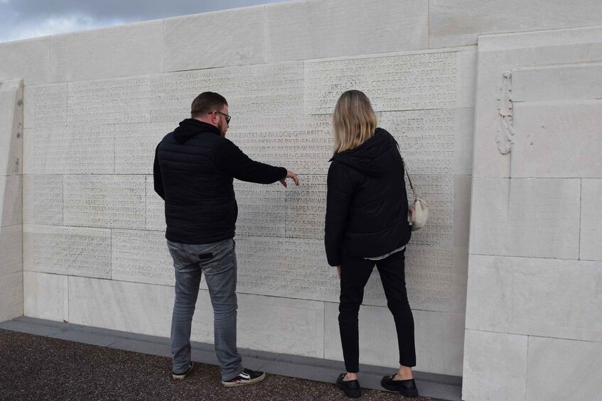 Two people examining a large stone wall with engraved names. 2