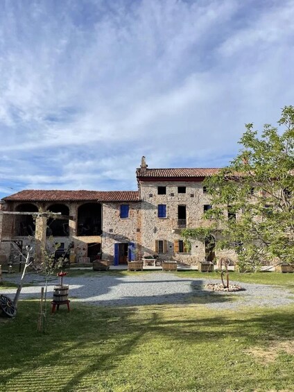 A stone building with a tiled roof, a gravel courtyard, and a tree. 3
