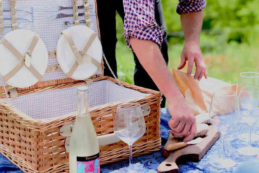 A picnic setup with a wicker basket, wine bottle, and a loaf of bread on a table. 2