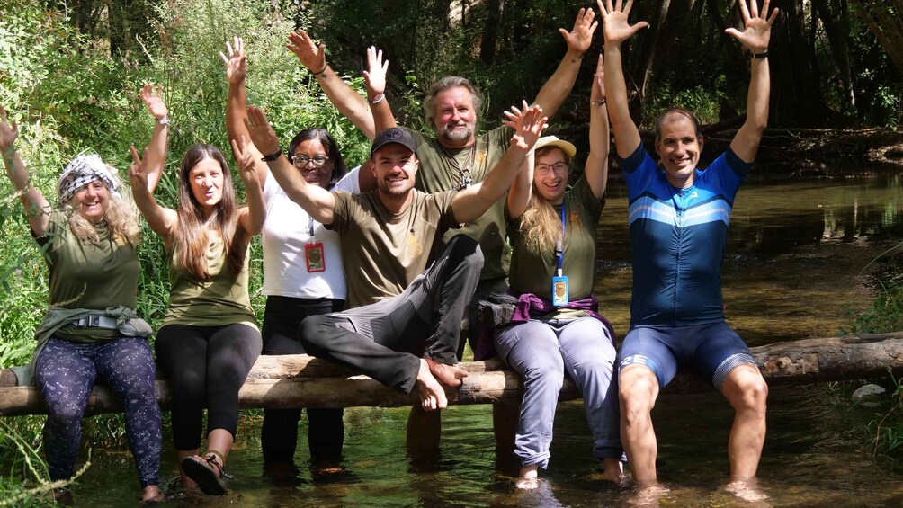 A group of people sitting on a log by a stream in a forest. 1