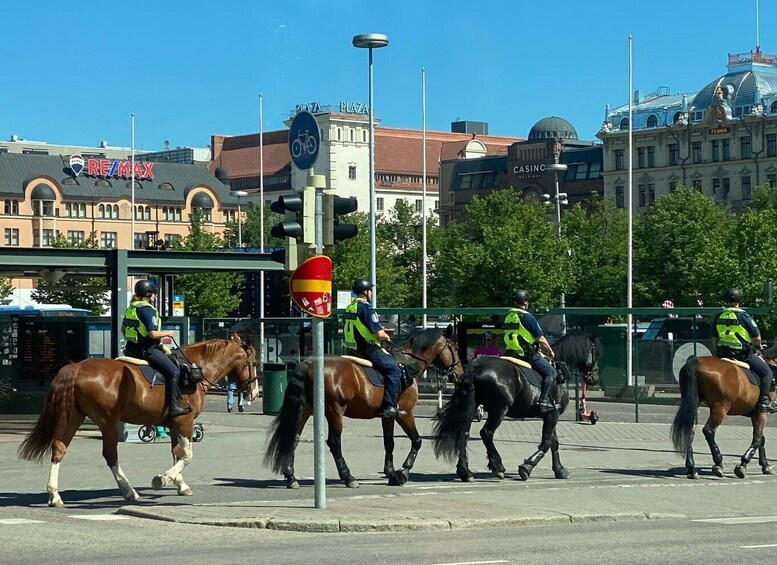 A street scene with horses and riders, a traffic light, and buildings in the background. 4