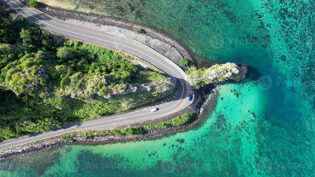 A winding road curving through a coastal area with clear turquoise waters and lush greenery. 2