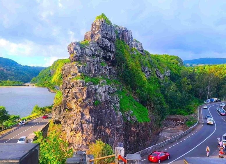 A coastal road with a prominent rocky cliff and a body of water in the background. 1