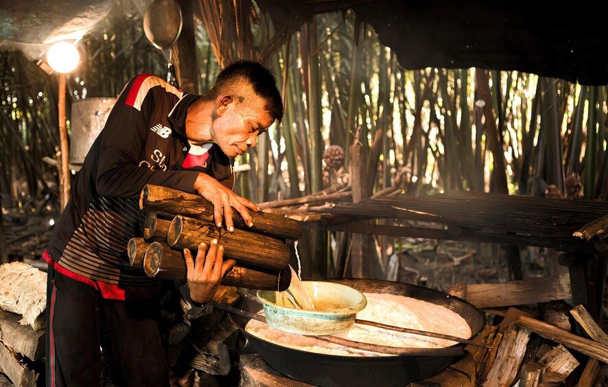 A person handling logs near a cooking area with a pot and a bowl. 3