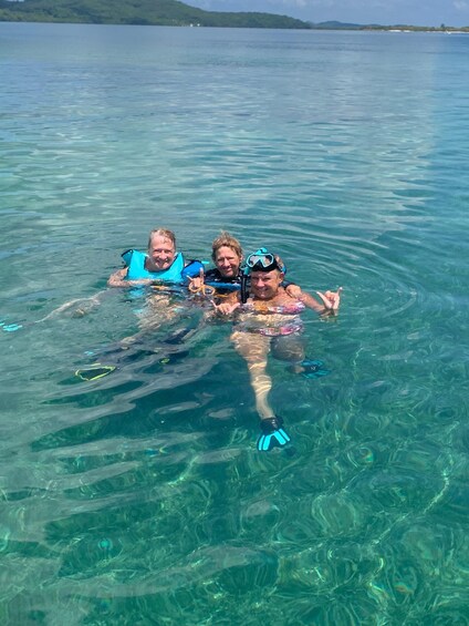 Three people snorkeling in clear blue water with a distant shoreline. 2