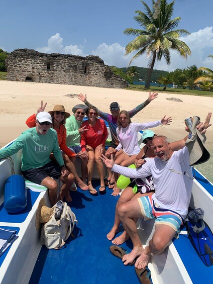 A group of people on a boat with a beach and palm trees in the background. 1