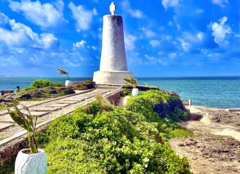 A coastal monument with a statue, surrounded by greenery and a clear blue sky. 2