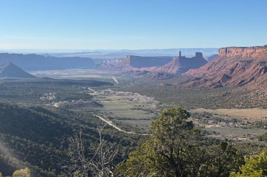 A canyon landscape with a winding road, distant mountains, and sparse vegetation. 1