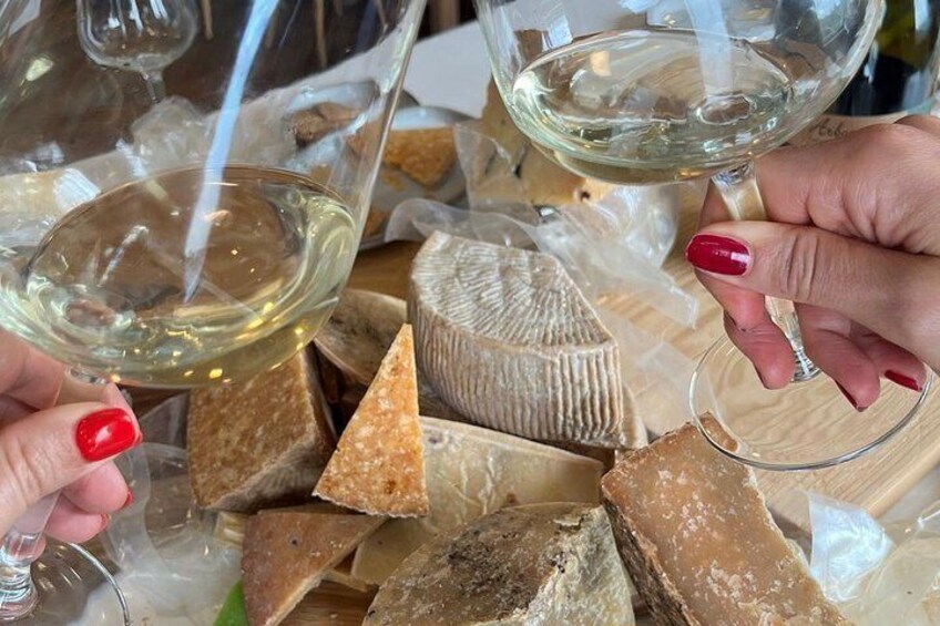 A person holding a glass of white wine, surrounded by various types of cheese. 4